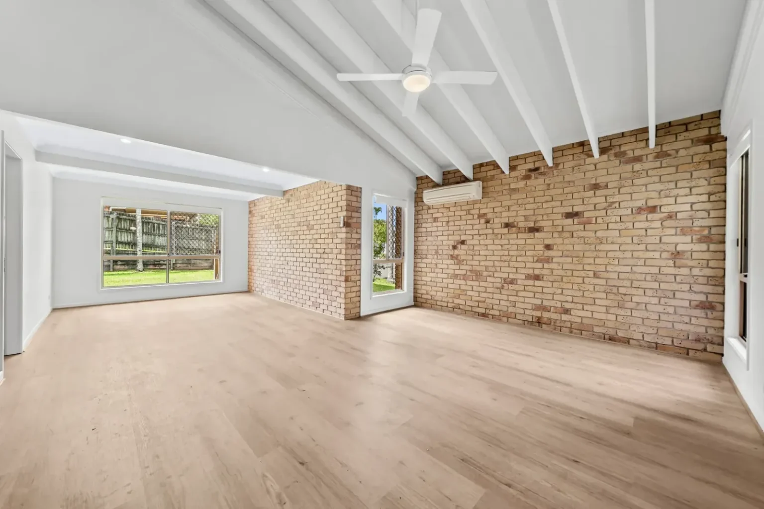 Unfurnished living room with raked ceiling and brick wall on BestBuys Neutral Oak hybrid flooring